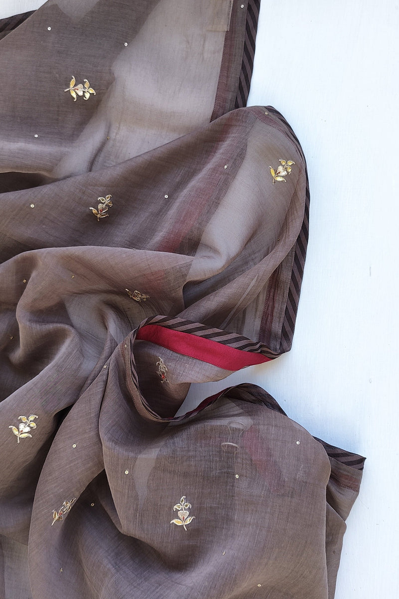 Dark brown fabric with gold gotapatti embroidery and a red ribbon on a white background.